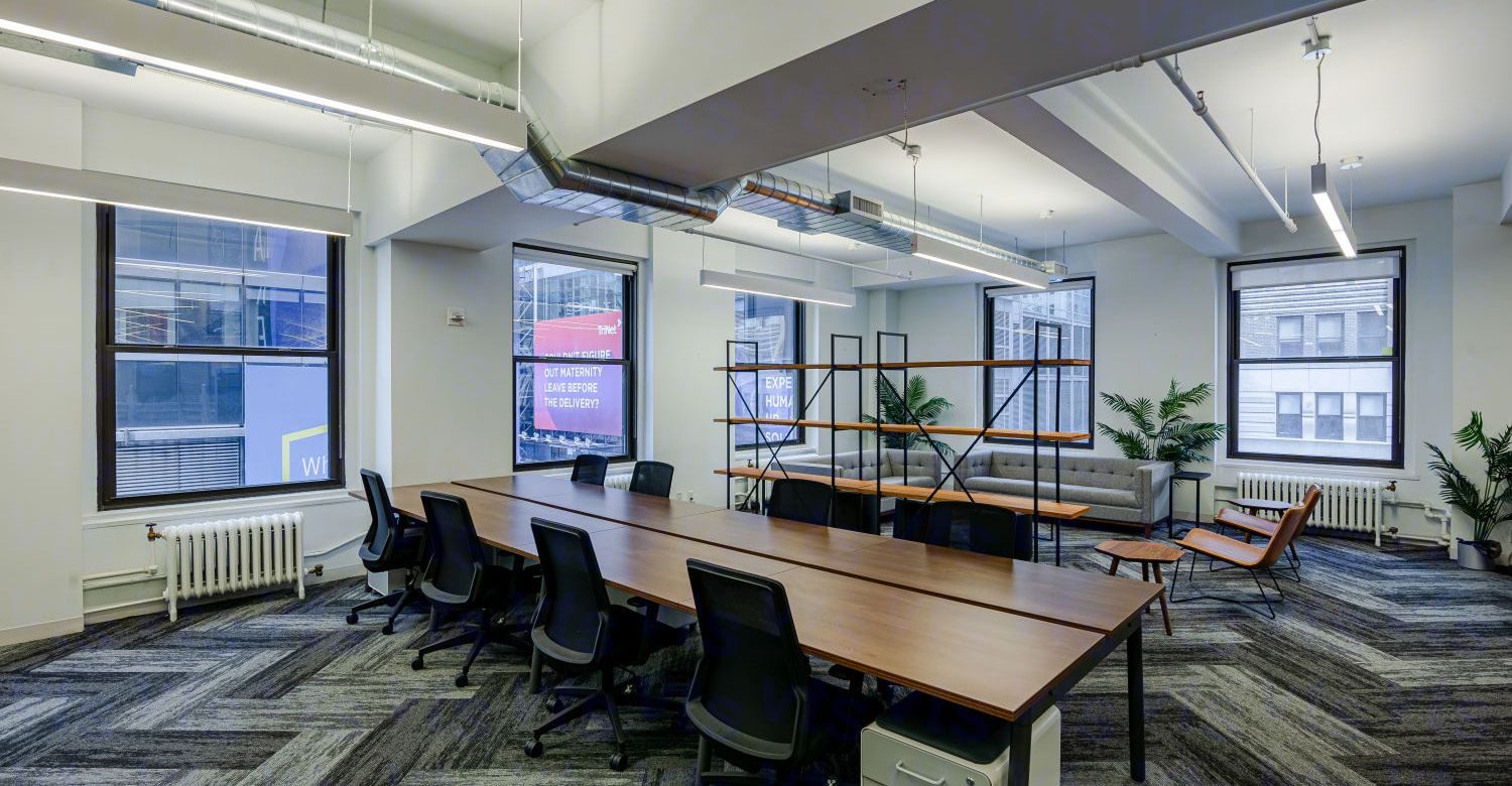 Bench desks with a lounge area and windows beyond